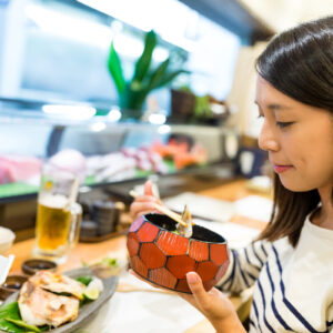 アジア人女性が日本食丼ぶりを食べている写真