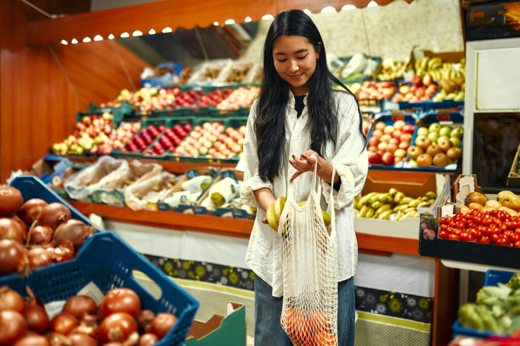 Young cute asian woman in white shirt puts bananas in shopper bag